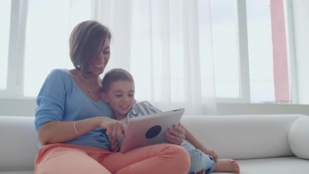 엄마와 아들 디지털 태블릿을 사용 하 여 소파에 앉아. 행복 한 엄마와 리틀 보가를 사용 하 여 비디오를 보고 함께 터치 스크린 태블릿. 웃 고 있는 어머니와 디지털 태블릿에 귀여운 소년 — 비디오