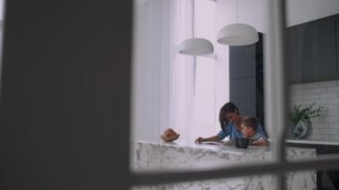 Oğlu masada oturan genç bir Ispanyol anne çocuk yardım ve oğlu soran okumayı öğretir,