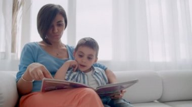 Mutlu anne ve çocuk oğlu okuma kitap yatakta gülüyor. Mutlu aile anne ve çocuk oğul okuma tutan kitap yatakta yatarken, gülümseyen anne bebek bakıcısı.