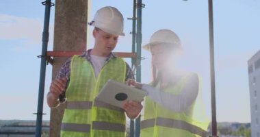 İnşaat sitesi takım veya mimar ve kurucu veya işçi kask ile bir iskele inşaat planı veya plan veya kontrol listesi üzerinde tartışmak.