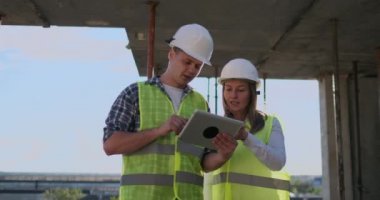 İki mühendis bir adam ve bir inşaat yerinde tablet bilgisayar ile bir kadın binanın inşaat planını kınaz