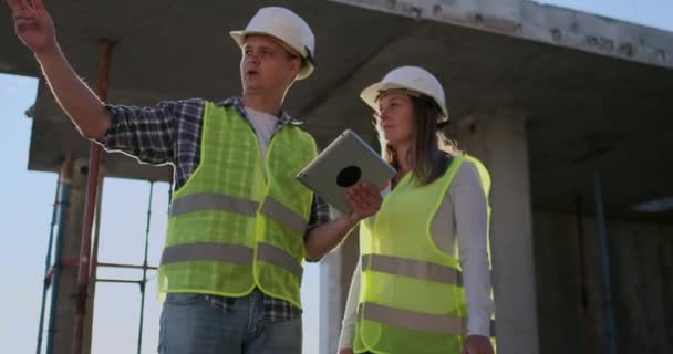 Professional engineers in safety vests and helmets working with digital tablet and blueprints. — Stock Video