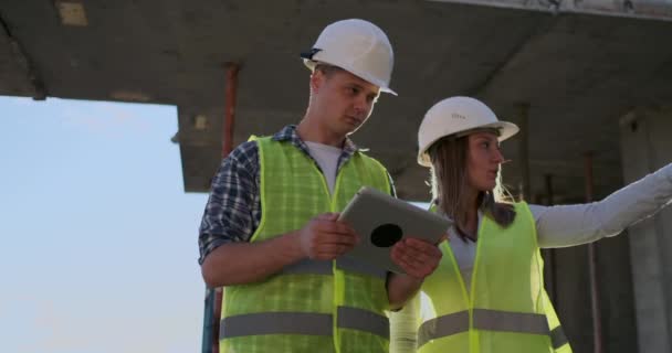 Két mérnök egy férfi és egy nő egy tabletta számítógép egy építkezésen elítélik az építési terv az épület — Stock videók