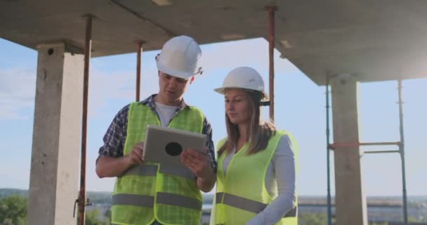 Professionele ingenieurs in Veiligheidsvesten en helmen werken met digitale Tablet PC- en blauwdrukken. — Stockvideo