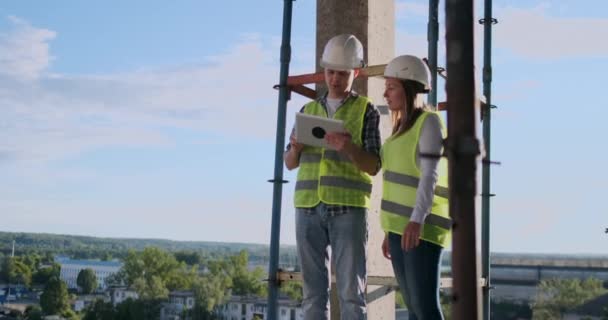 İki mühendis bir adam ve bir inşaat yerinde tablet bilgisayar ile bir kadın binanın inşaat planını kınaz — Stok video