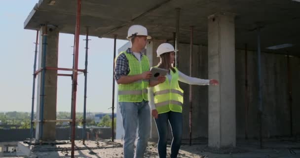 Руководитель строящегося здания мужчина обсуждает с инженером-конструктором ход строительства и рассматривает план строительства — стоковое видео