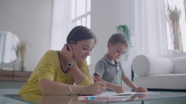 Beyaz odada ayna masada oturan anne ve oğul gülümseyen ve gülüyor renkli kalemler ile berabere.