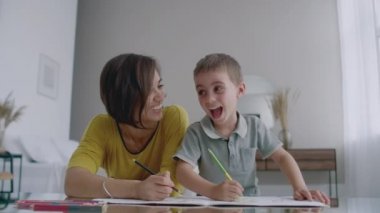 Oğlumla işaretleri ile ailesi tasvir kağıt üzerine çizim yerde yatarken bir sıcak kazaklı güzel genç anne. Çocuk öğrenir çizmek için.
