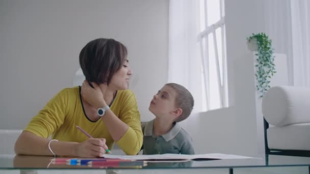 Schöne junge Mutter in einem warmen Pullover auf dem Boden liegend, während mein Sohn mit Filzstiften auf Papier zeichnet, die seine Familie darstellen. das Kind lernt zeichnen. — Stockvideo