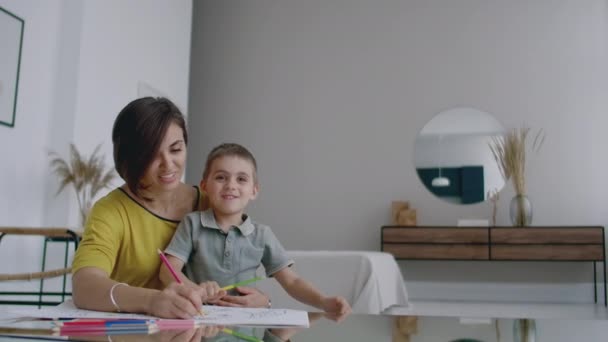 Maman et son fils assis à la table miroir dans la salle blanche dessinent avec des crayons de couleur souriant et riant . — Video