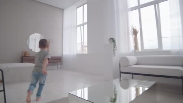 Mutter und Sohn haben Spaß beim Nachholspiel zu Hause in einem weißen Interieur. mit dem Kind im Haus herumlaufen und Verstecken spielen. — Stockvideo
