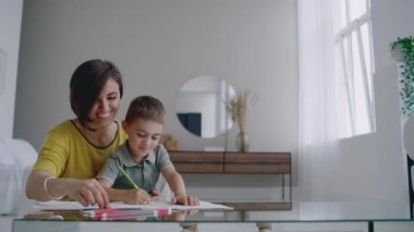 Oğlumla işaretleri ile ailesi tasvir kağıt üzerine çizim yerde yatarken bir sıcak kazaklı güzel genç anne. Çocuk öğrenir çizmek için.