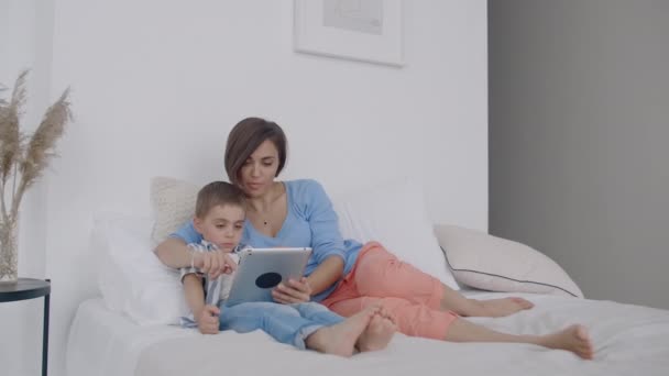 Μητέρα και γιος χρησιμοποιώντας ψηφιακό δισκίο στο υπνοδωμάτιο στο σπίτι. Μπροστινή όψη του Happy Καυκάσιος μητέρα και γιος χρησιμοποιώντας ψηφιακό δισκίο στο υπνοδωμάτιο στο σπίτι. — Αρχείο Βίντεο