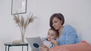 Anne ve oğlu evde yatak odasında dijital tablet kullanarak. Evde yatak odasında dijital tablet kullanarak mutlu Kafkas anne ve oğlu ön görünümü.