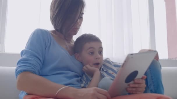 幸福的家庭妈妈和孩子的儿子使用数字平板电脑坐在屏幕上,微笑的家长母亲与孩子儿子拿着电脑看屏幕做网上购物视频调用看卡通. — 图库视频影像