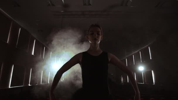 SLOW MOTION: prima ballet ensaia uma performance solo em pé no palco do teatro em fumaça em um vestido preto na luz — Vídeo de Stock