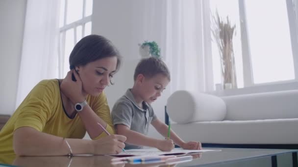 Jeune femme et enfant dessinant ensemble faisant l'image avec des crayons dans plat . — Video