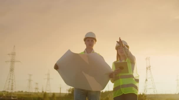 İki elektrikçi birlikte çalışıyor, kasklarla elektrik iletim hattının yanında duruyorlar. Güç iletimi ile yakın alanda duran — Stok video