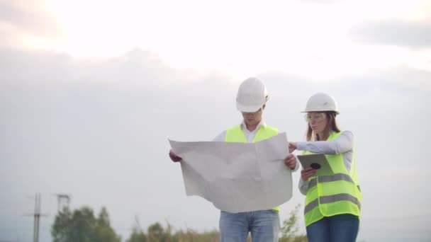 Coworking-Ingenieure mit Tablets auf Solaranlage. Erwachsene Männer und Frauen in Harthüten benutzen Tablets, während sie im Freien auf einer Trafostation stehen. Transport sauberer Energie — Stockvideo