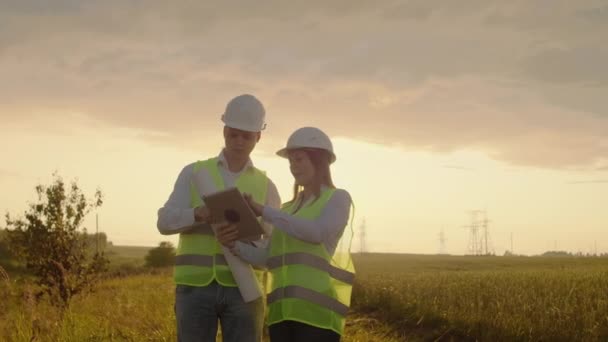 Um grupo de engenheiros em uma usina de alta tensão com um tablet e desenhos caminhar e discutir um plano para o fornecimento de eletricidade para a cidade. Transporte de energias limpas renováveis — Vídeo de Stock