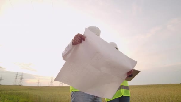 Two electricians work together, standing in the field near electricity transmission line in helmets. Standing in the field near with power transmission — Stock Video