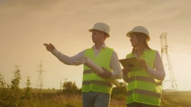 Güneş enerjisi santralinde tabletleri olan ortak çalışma mühendisleri. Yetişkin erkek ve kadınlar trafo platformunda açık havada dururken tablet kullanarak hardhats. Temiz enerji nin taşınması