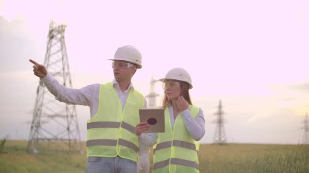 Un groupe d'ingénieurs dans une centrale électrique à haute tension avec une tablette et des dessins marchent et discutent d'un plan pour l'approvisionnement en électricité de la ville. Transport d'énergies propres renouvelables — Video