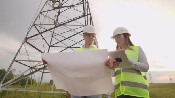 Un grupo de ingenieros en una planta de energía de alto voltaje con una tableta y dibujos caminan y discuten un plan para el suministro de electricidad a la ciudad. Transporte de energía limpia renovable — Vídeo de stock