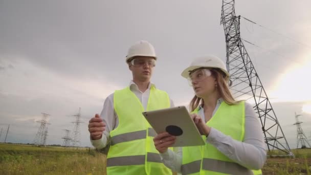 Ein Elektriker männlich und weiblich auf den Feldern in der Nähe der Hochspannungsfreileitung. er ist ein Elektriker, der den Prozess der Errichtung von Stromleitungen verwaltet. — Stockvideo