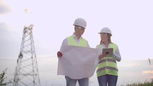 Un grupo de ingenieros en una planta de energía de alto voltaje con una tableta y dibujos caminan y discuten un plan para el suministro de electricidad a la ciudad. Transporte de energía limpia renovable — Vídeo de stock