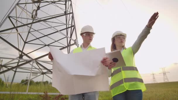 Een elektricien man en vrouw in de velden in de buurt van de kracht transmissielijn. Hij is een elektricien die het proces van het oprichten van stroomlijnen beheert. — Stockvideo