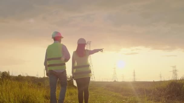 A vista da parte de trás: grupo de engenheiros em uma usina de alta tensão com um tablet e desenhos caminhar e discutir um plano para o fornecimento de eletricidade para a cidade . — Vídeo de Stock