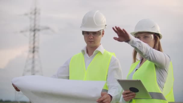 Engineers in uniform working with a laptop near transmission lines — Stock Video