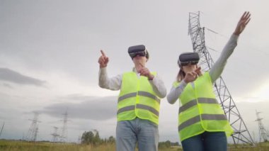 Vr gözlük bir adam ve bir kadın mühendis yüksek voltaj kabloları ile elektrik kuleleri arka plan karşı elektrik dağıtım ve elektrik dağıtımı kontrol.