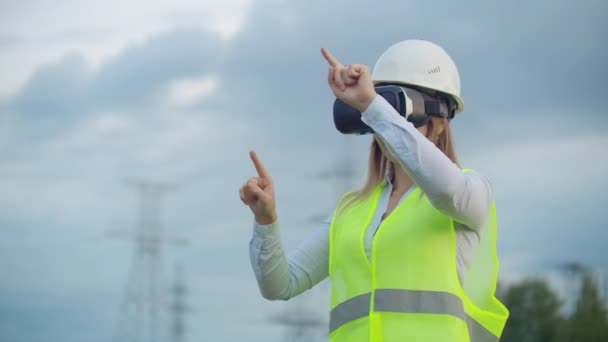 Retrato de una mujer moderna de la Contraloría del ingeniero realizando la inspección a través de gafas de realidad virtual y un casco blanco, vestido de uniforme en el fondo las torres de poder — Vídeos de Stock