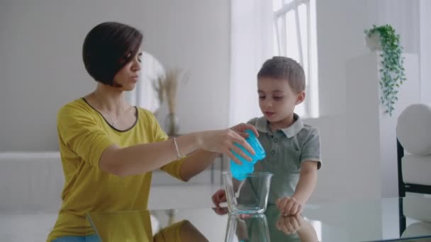 Anne ve oğlu masada oynarken yerde oturan ve elastik bir oyuncak kullanarak gülüyor — Stok video