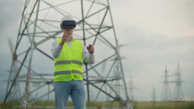 Sanal gerçeklik gözlük bir erkek elektrikçi yüksek voltajlı elektrik iletim hatları arka plan karşı güç santralinin grafik arayüzü ile iş simüle elini hareket ettirir