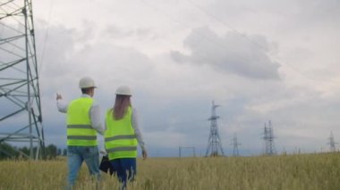 Arkadan görünüm: bir tablet ve çizimler ile yüksek voltajlı bir elektrik santralinde mühendis grubu yürümek ve şehre elektrik arzı için bir plan tartışmak.