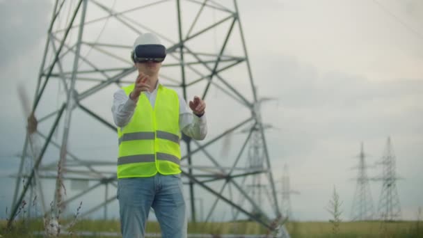 Sanal gerçeklik gözlük bir erkek elektrikçi yüksek voltajlı elektrik iletim hatları arka plan karşı güç santralinin grafik arayüzü ile iş simüle elini hareket ettirir — Stok video