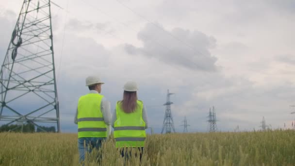 La vista desde atrás: grupo de ingenieros en una central eléctrica de alto voltaje con una tableta y dibujos caminan y discuten un plan para el suministro de electricidad a la ciudad . — Vídeo de stock