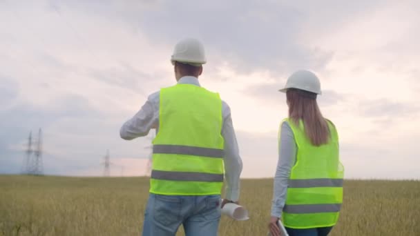 La vista dal retro: gruppo di ingegneri in una centrale ad alta tensione con tablet e disegni a piedi e discutere un piano per la fornitura di energia elettrica alla città . — Video Stock