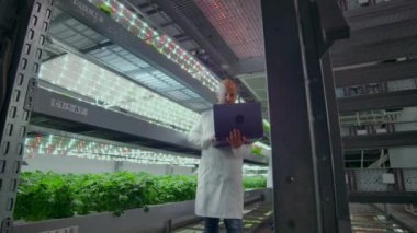 Beyaz önlüklü mikrobiyoloji, test sonuçlarını inceleyen dizüstü bilgisayarlar ve tabletlerle modern bir çiftliğe gidiyor ve yeni bitki türlerinin incelenmesi için numune topluyor..