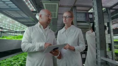 Dizüstü bilgisayarlı beyaz önlüklü bilim adamları çiftliğin koridoruna hidroponiklerle birlikte giderler ve bitkiler üzerindeki gen çalışmalarının sonuçlarını tartışırlar. Örneklere bak..