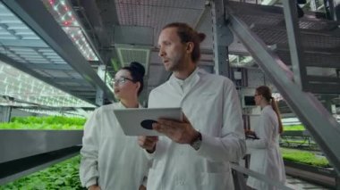 Beyaz önlüklü mikrobiyoloji, test sonuçlarını inceleyen dizüstü bilgisayarlar ve tabletlerle modern bir çiftliğe gidiyor ve yeni bitki türlerinin incelenmesi için numune topluyor..