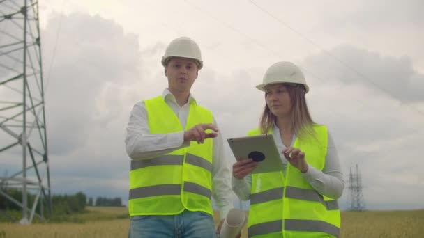 Stromleitungen, ein Mann und eine Frau mit einem Tablet in der Hand diskutieren über den Fortschritt des Bauprojekts. — Stockvideo