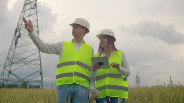 Un electricista en los campos cerca de la línea de transmisión de energía. El electricista maneja el proceso de erigir líneas eléctricas. El mecánico en un casco . — Vídeos de Stock