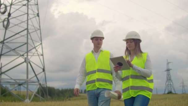 Líneas eléctricas, un hombre y una mujer ingenieros con una tableta en sus manos discutiendo el progreso del proyecto de construcción . — Vídeo de stock
