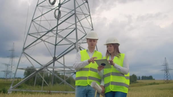 Líneas eléctricas, hombres y mujeres ingenieros con una tableta en sus manos comprueban el progreso de la instalación de nuevas torres y analizan la red . — Vídeo de stock