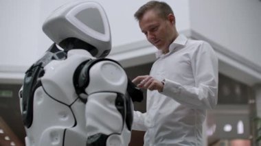 Alışveriş merkezindeki adam bir robot danışmanla iletişim kuruyor. Modern dükkan ve robot satıcısı. Robot Alışveriş Merkezi'nde bir adam yardımcı olur