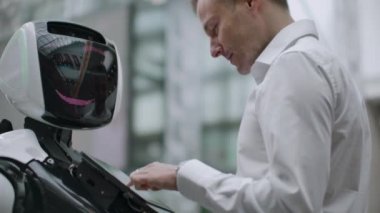 Bir adam bir robot bot ile duruyor ve ona sorular sorar ve robot gövdesi üzerinde ekrana tıklayarak yardım ister.